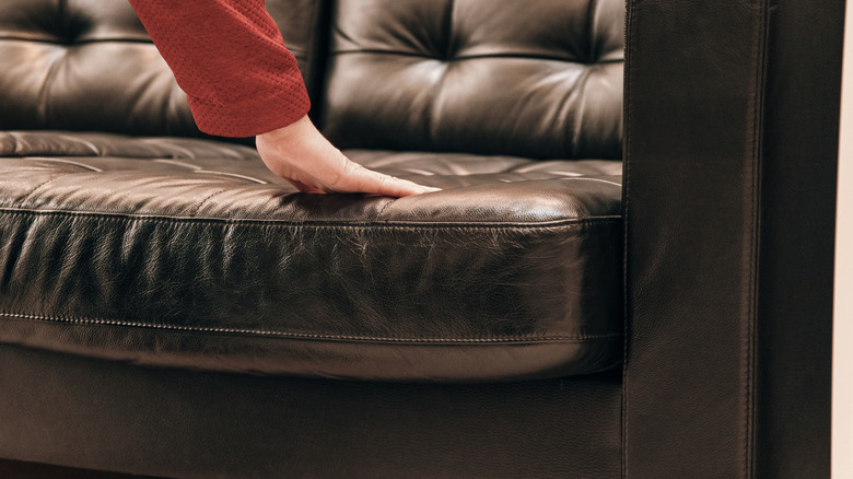 A woman's hand inspecting a brown leather sofa