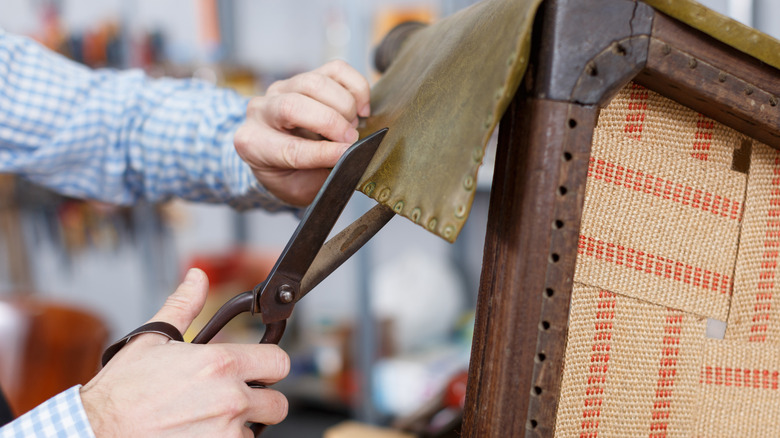 A man cuts leather to reupholster an antique chair