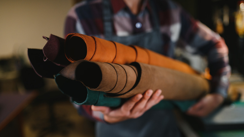 A leather craftsman holds several rolls of leather