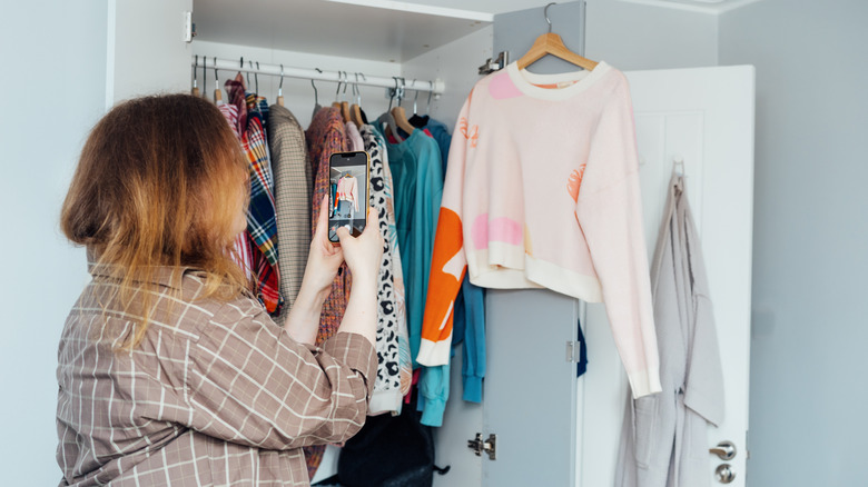 Woman taking photos of clothes hanging in wardrobe
