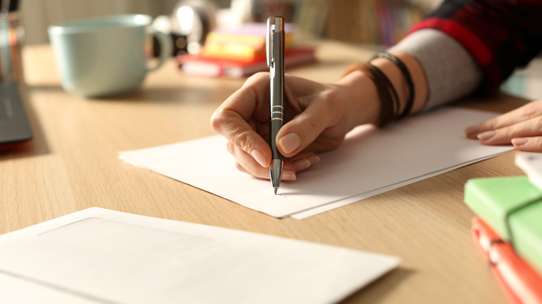 Hand holding a pen and writing on a blank piece of paper