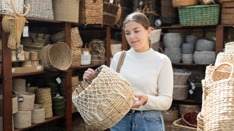 Woman in white sweater examining a wicker basket for durability before buying