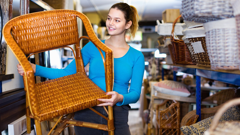 Smiling woman lifting a wicker chair at a thrift shop