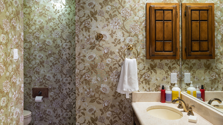 Outdated 1960s vintage bathroom with green floral wallpaper and wood cabinet