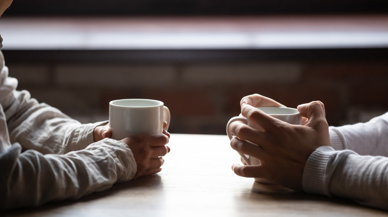 hands holding coffee mugs on table