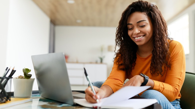 woman writing and smiling with computer