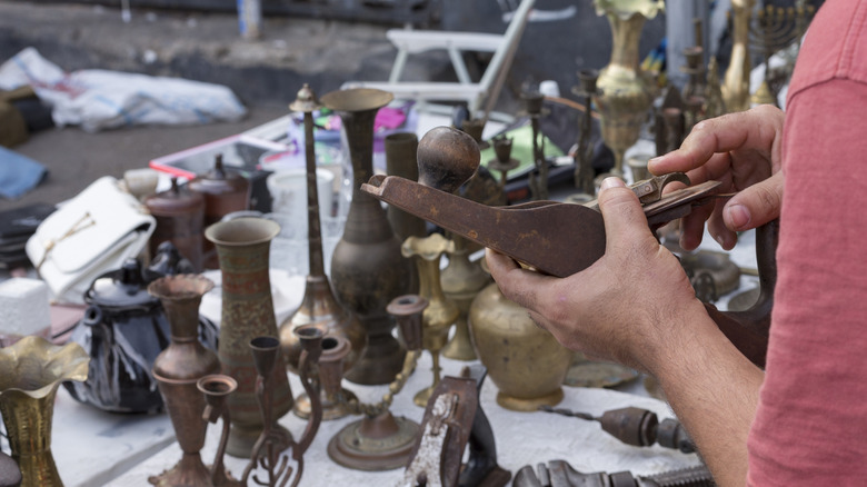 A person holds an old plane above some rusty tools and other trinkets on a vendor's table at a flea market.
