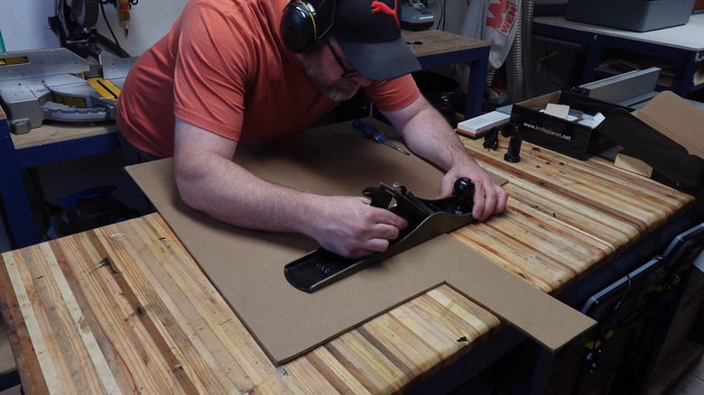 A man wearing ear protection cuts some plywood using an old Stanley No. 6 plane.