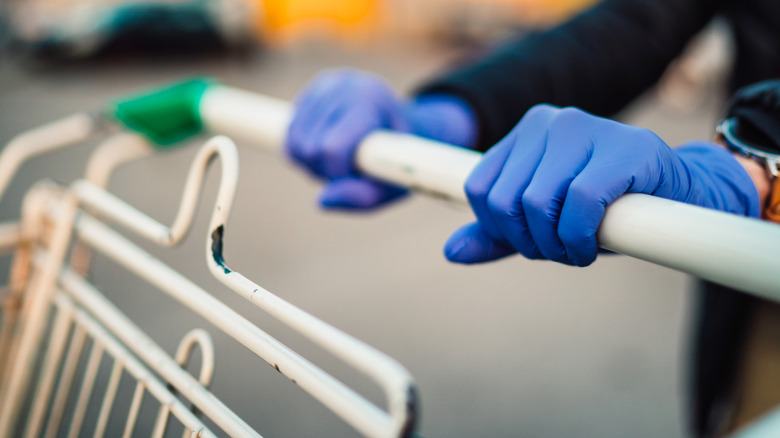Close-up view of hands in rubber gloves pushing shopping cart