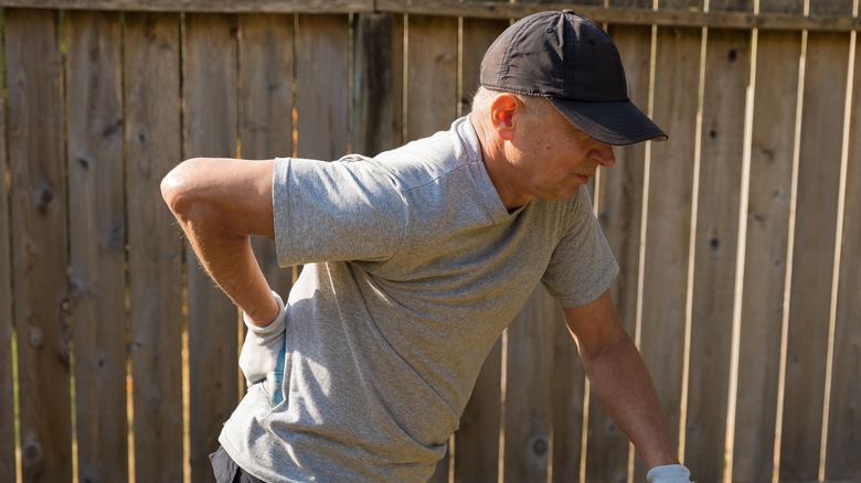 A man holds his back while standing in front of a fence
