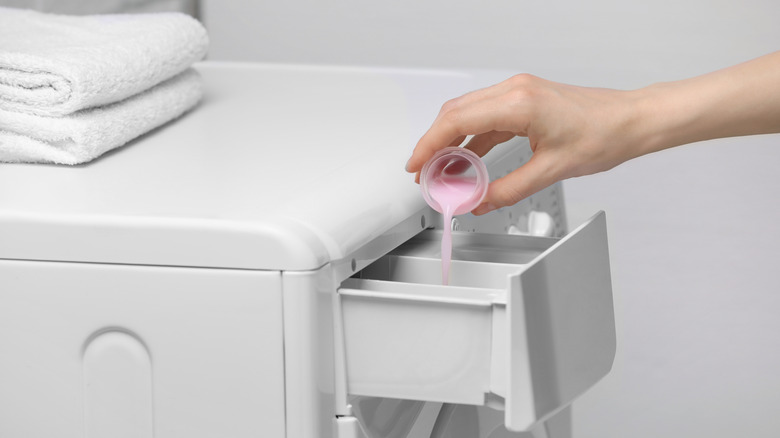Hand adding fabric softener to white washing machine