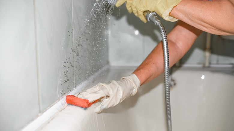 gloved hand cleaning shower corner