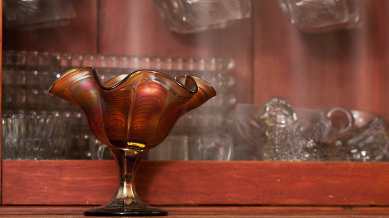 carnival glass piece on wood china cabinet with other glass behind it