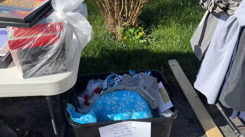 Items bundled in bags on a white table and a bin of items sold as a lot