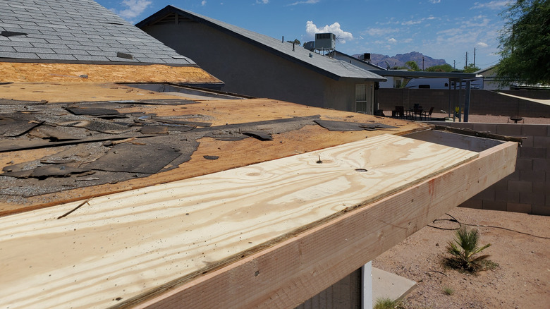 A roof with newly laid boards and part of the roof with shingles removed.