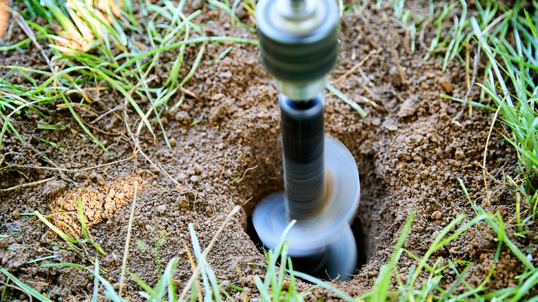 A garden auger being used to make holes in the ground for planting