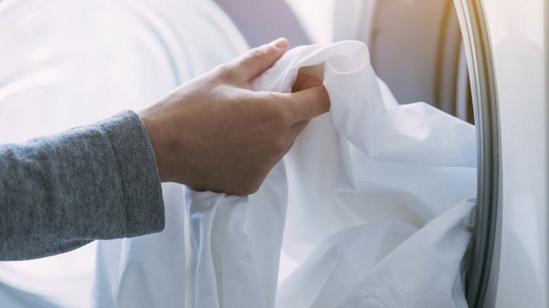 A hand pulls a white sheet out of the dryer.