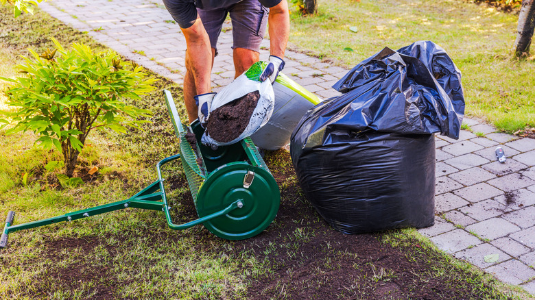 A gardener pours compost into a topdresser to spread on his lawn.