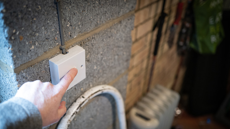 A person holding his finger over the light switch in a residential garage.