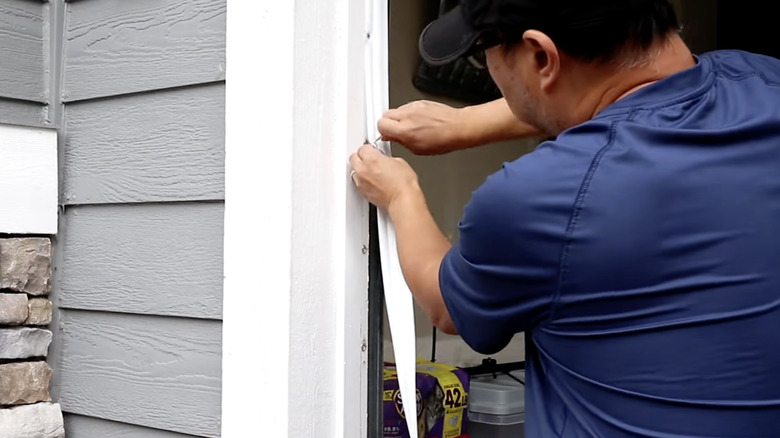 A person installs weatherstripping around the sides of a garage door.