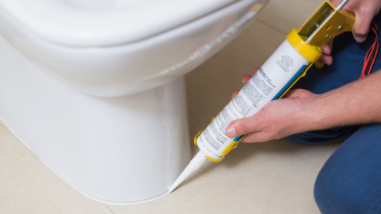 A person caulks a toilet base using a caulking gun.