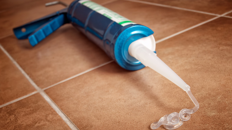 Clear silicone caulk leaks out of a nozzle on a tube in a blue caulking gun.