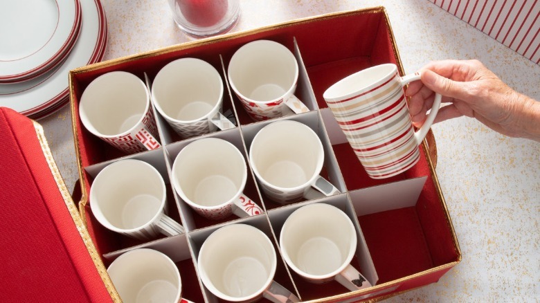 person putting coffee mugs into red fabric divided organizer case