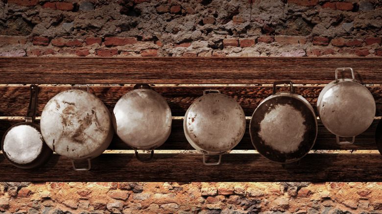 A row of pots and pans hanging on a rustic slatted wall