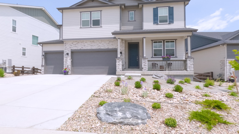 A recently built home in a suburban neighborhood with gray exterior coloring an gravel rock landscaping