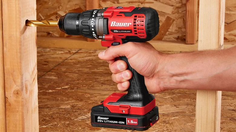 A hand holding a Bauer cordless drill and drilling into a wall stud