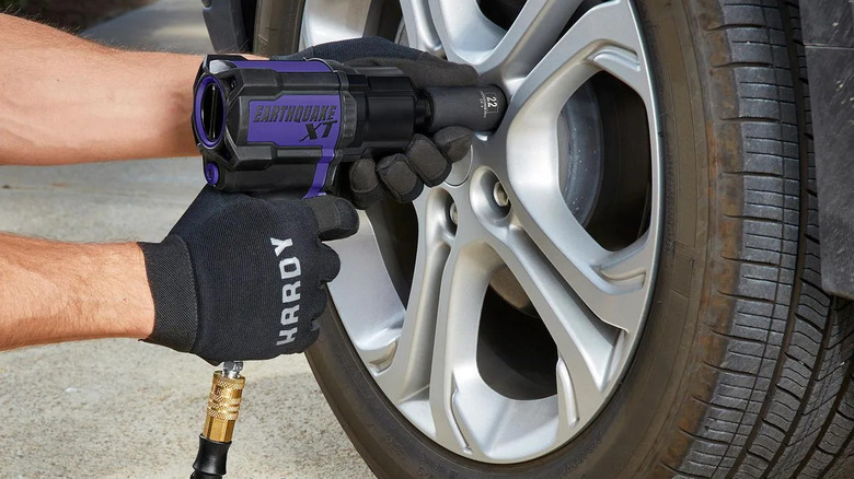 A person's gloved hands using an Earthquake XT air impact wrench to secure lug nuts