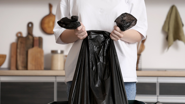 Close-up of person taking out black trash bag from kitchen