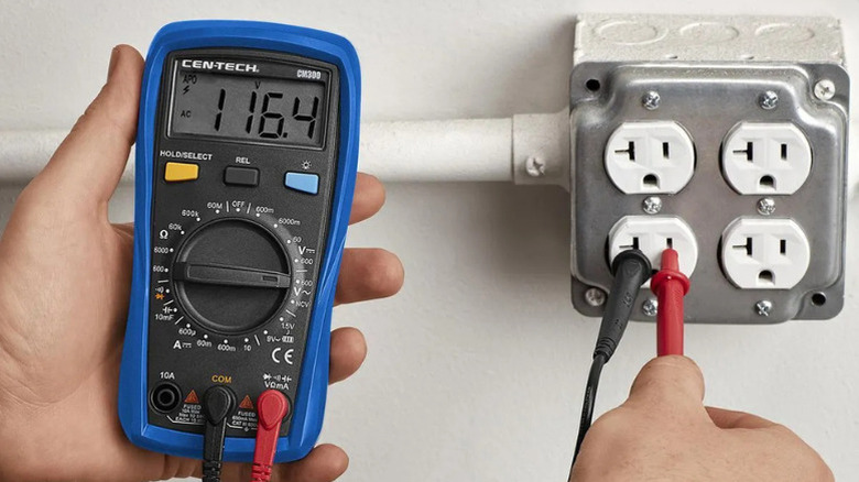 Close-up of a person using Cen-Tech's 9-Function Digital Multimeter to test an electrical outlet