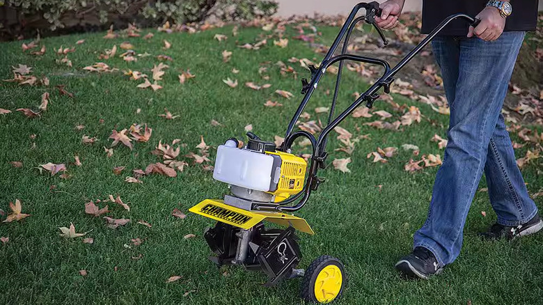 A man walks behind a Champion Power Equipment Portable Gas Garden Tiller Cultivator