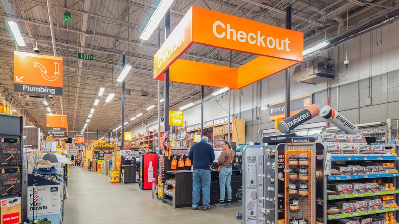 Home Depot customers stand under a large orange sign reading 'Checkout'