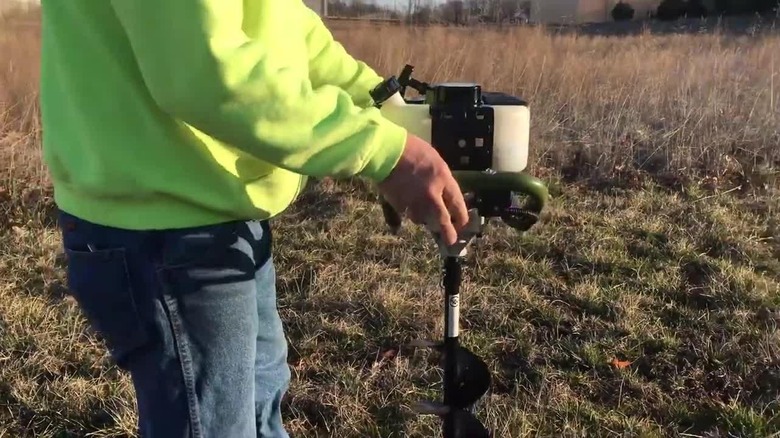 A man uses a Sportsman Earth Series Gas Powered Auger to drill holes in the ground