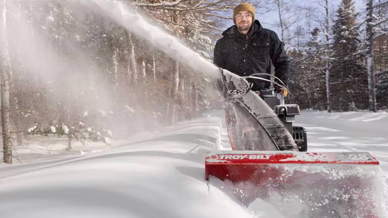 A man uses a Troy-Bilt Storm Electric Start Gas Snow Blower with Power Steering to clear a path in deep snow