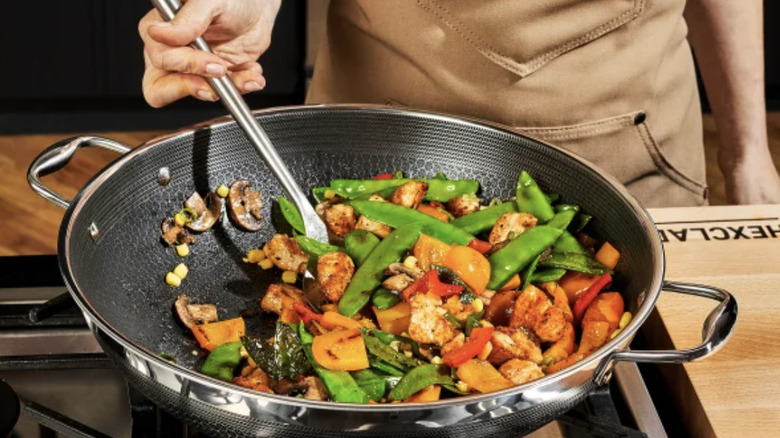 A person stir frying in a HexClad wok on a stove