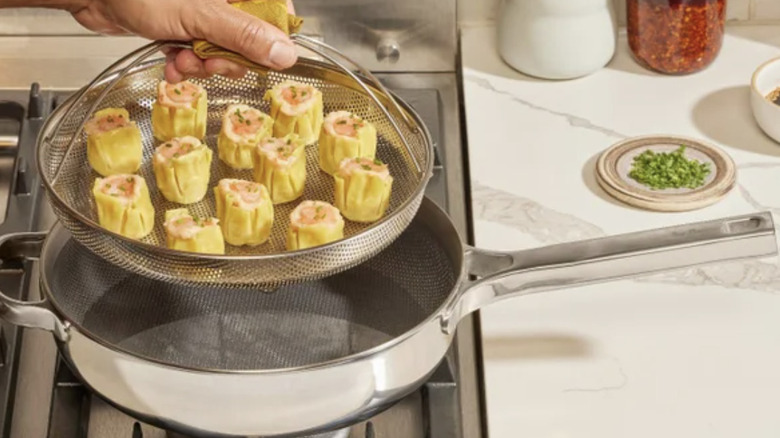A hand putting a basket of dumplings in a steamer pot on a stove