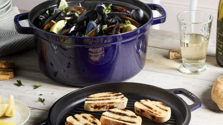 A blue dutch oven with muscles in it and a cast iron grille with bread that has grill marks