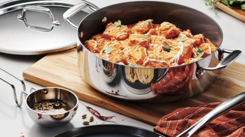 Tramontina caserole pit with creamy chicken on a cutting board next to the pot lid, a tadaka with oil in it, and a flat pan