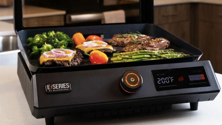 Blackstone E-series griddle on a counter cooking burgers, steak, and veggies
