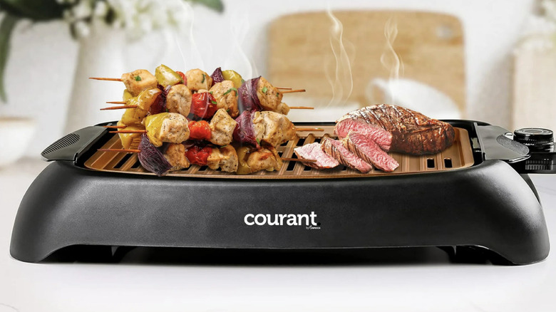 Courant griddle with steak and kabobs on a counter in front of plants and a cutting board