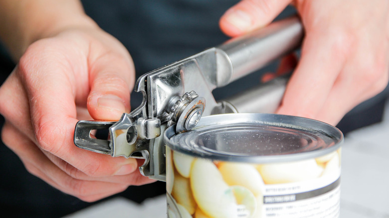 A person using a can opener to open a can of beans