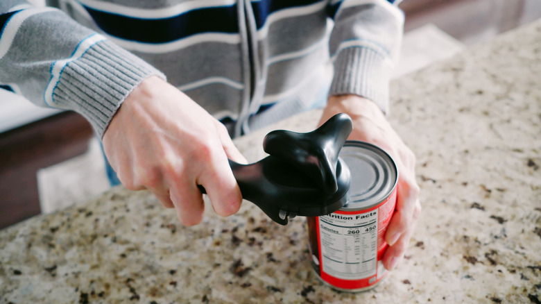 Person opening a can with a manual can opener