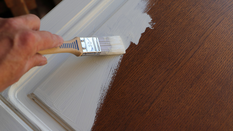 Brown wooden cabinet door being painted with white paint