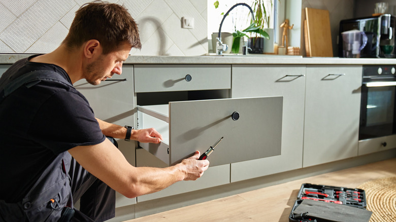 A man holding a screwdriver while installing kitchen cabinet drawers