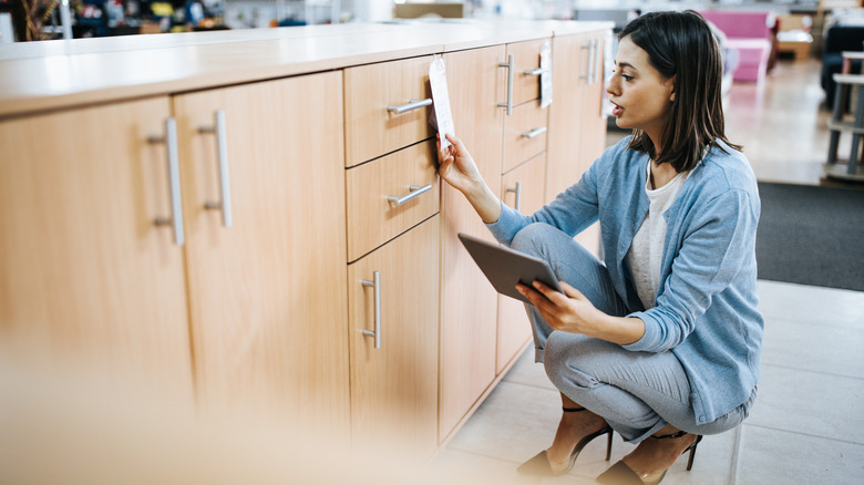 Woman looking at the price tag of base kitchen cabinets