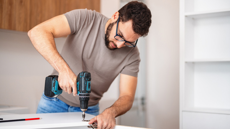 A person assembling kitchen cabinets with a drill