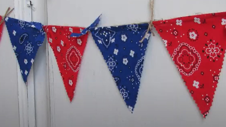 A blue and red bunting made of twine and bandanas decorate a white wall